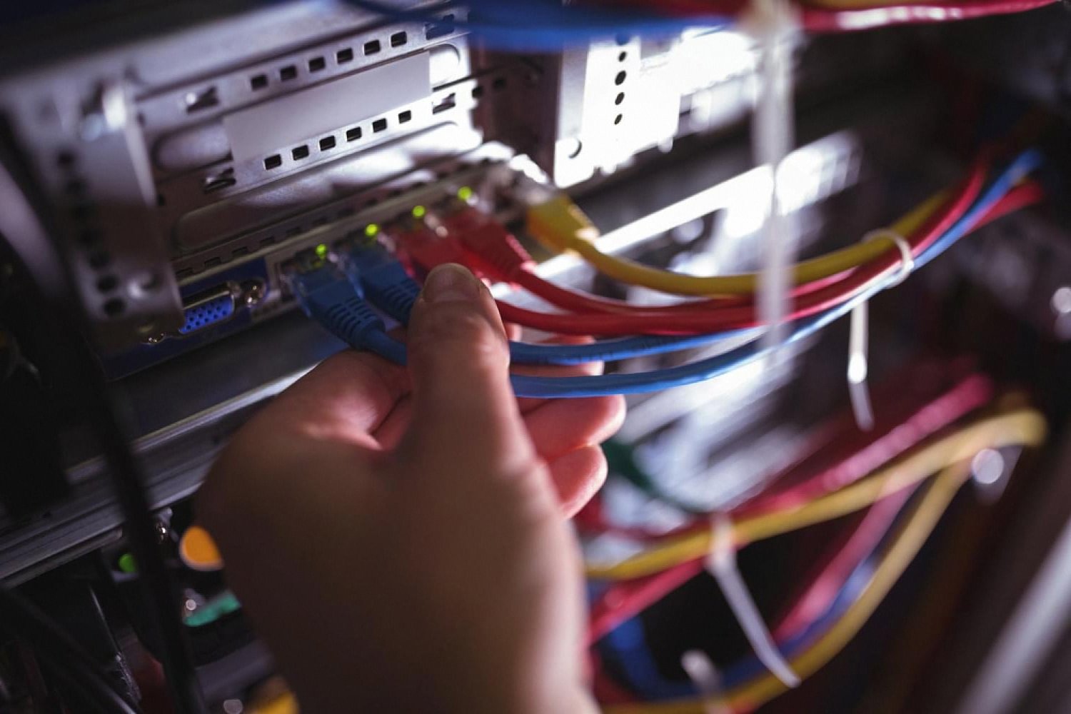 Hand connecting cables in a server rack, showing IT maintenance work in a Dubai data room