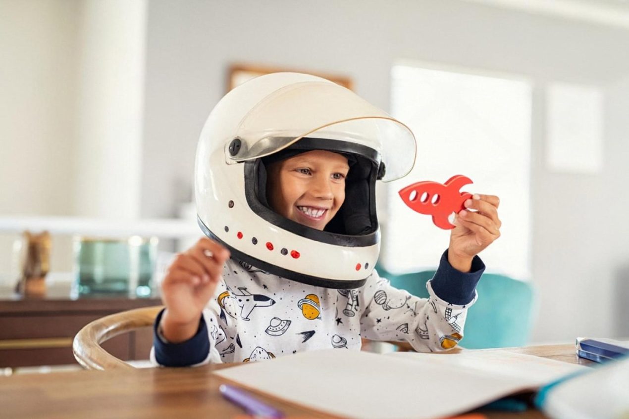 Young child wearing an astronaut helmet and holding a wooden rocket during imaginative play