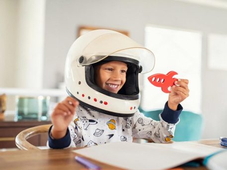 Young child wearing an astronaut helmet and holding a wooden rocket during imaginative play