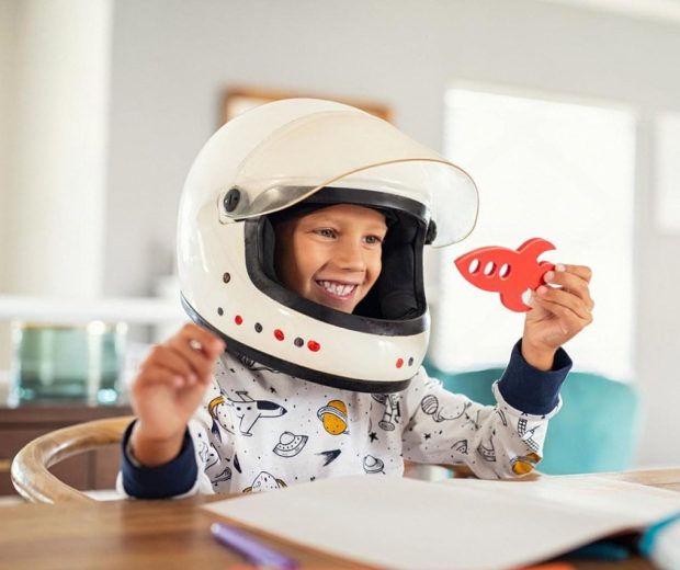 Young child wearing an astronaut helmet and holding a wooden rocket during imaginative play