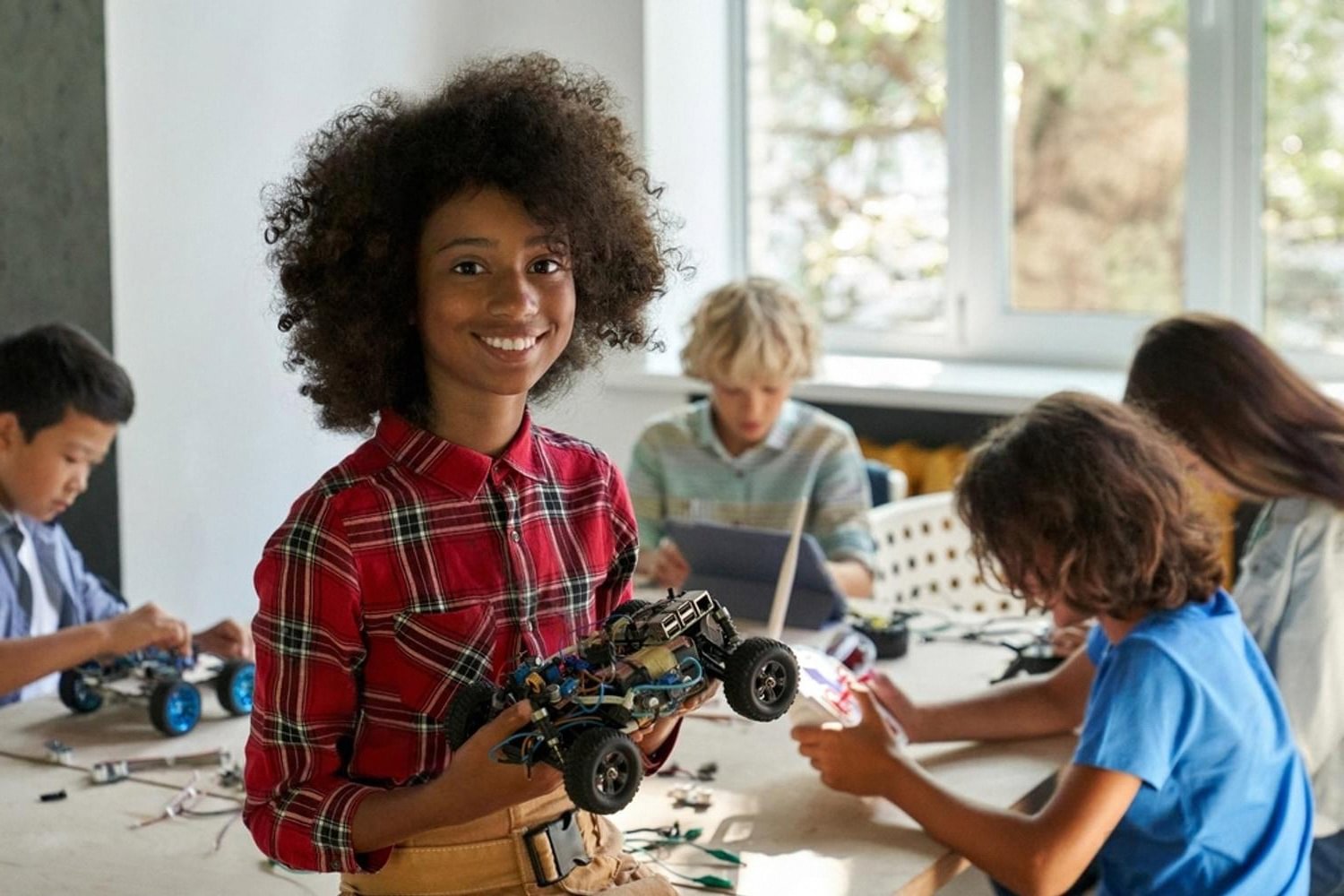 Girl smiling with a self-built model car alongside classmates working on STEM toys